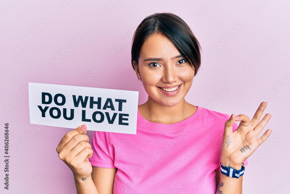 Beautiful young woman with short hair holding paper with do what you love text doing ok sign with fingers, smiling friendly gesturing excellent symbol Beautiful young woman with short hair holding paper with do what you love text doing ok sign with fingers, smiling friendly gesturing excellent symbol