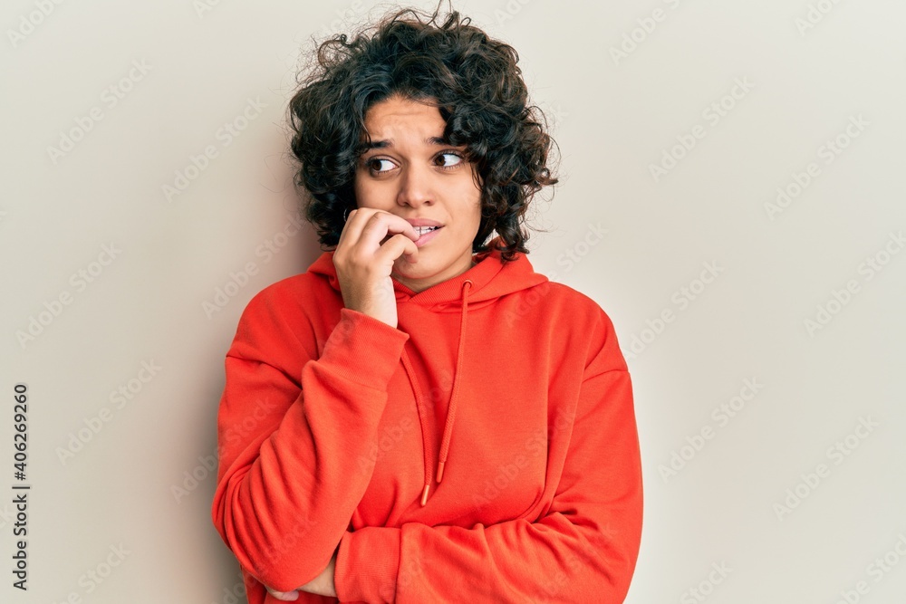 Young hispanic woman with curly hair wearing casual sweatshirt looking stressed and nervous with hands on mouth biting nails. anxiety problem. Young hispanic woman with curly hair wearing casual sweatshirt looking stressed and nervous with hands on mouth biting nails. anxiety problem.