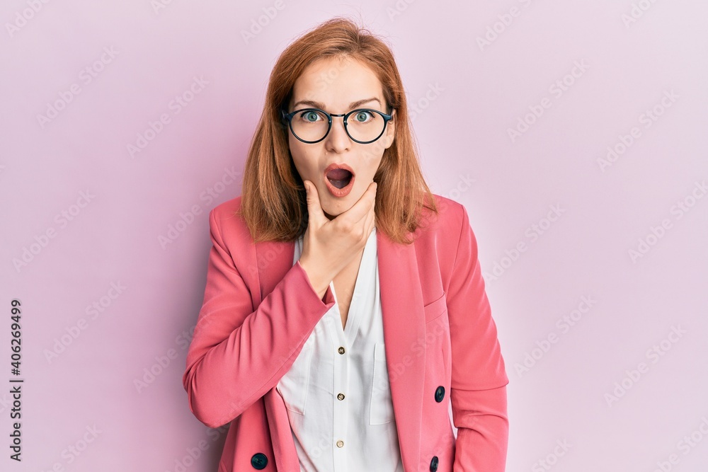 Young caucasian woman wearing business style and glasses looking fascinated with disbelief, surprise and amazed expression with hands on chin
