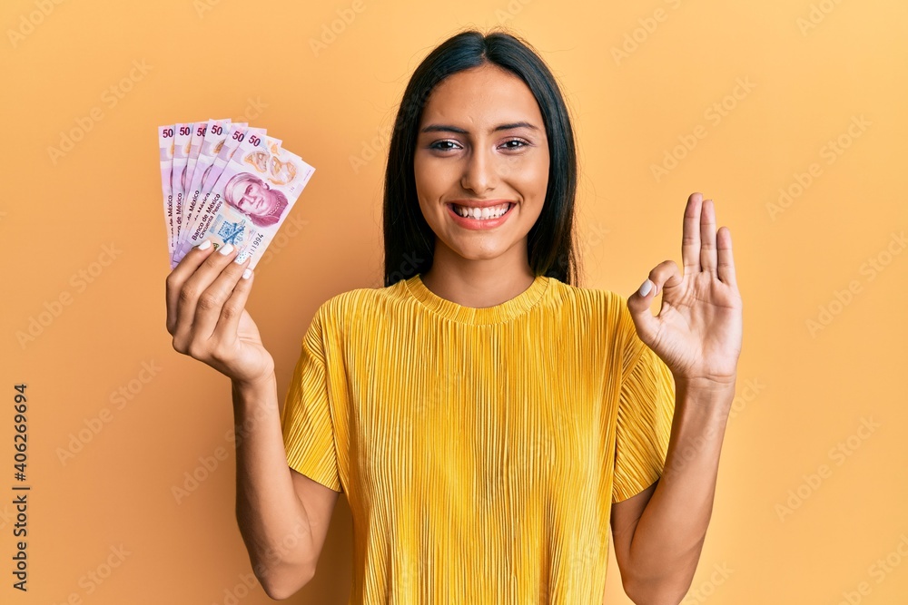 Young brunette woman holding 50 mexican pesos banknotes doing ok sign with fingers, smiling friendly gesturing excellent symbol Young brunette woman holding 50 mexican pesos banknotes doing ok sign with fingers, smiling friendly gesturing excellent symbol