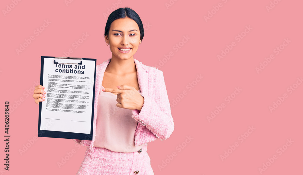 Young beautiful latin girl holding clipboard with terms and conditions document smiling happy pointing with hand and finger Young beautiful latin girl holding clipboard with terms and conditions document smiling happy pointing with hand and finger