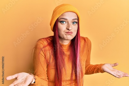 Young caucasian woman wearing wool cap clueless and confused expression with arms and hands raised. doubt concept. © Krakenimages.com