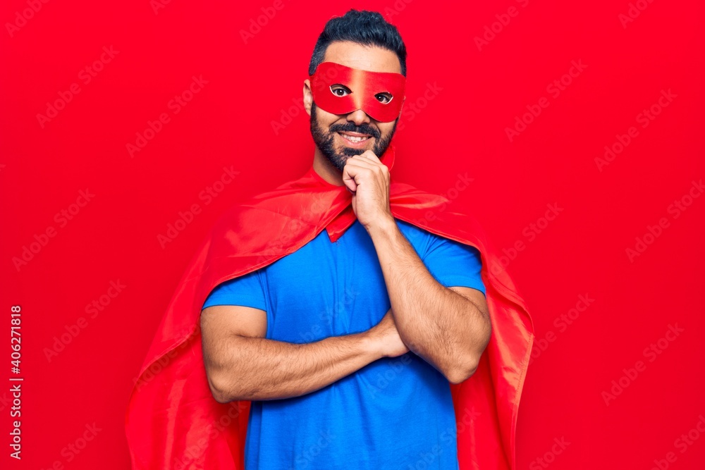 Young hispanic man wearing super hero costume smiling looking confident at the camera with crossed arms and hand on chin. thinking positive. Young hispanic man wearing super hero costume smiling looking confident at the camera with crossed arms and hand on chin. thinking positive.