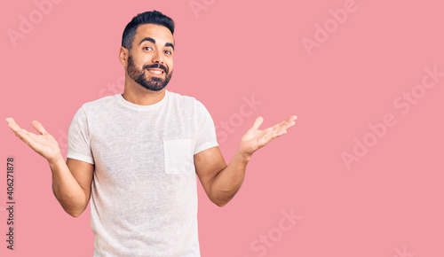 Young hispanic man wearing casual clothes clueless and confused expression with arms and hands raised. doubt concept.