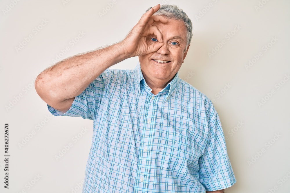 Senior grey-haired man wearing casual clothes smiling happy doing ok sign with hand on eye looking through fingers Senior grey-haired man wearing casual clothes smiling happy doing ok sign with hand on eye looking through fingers