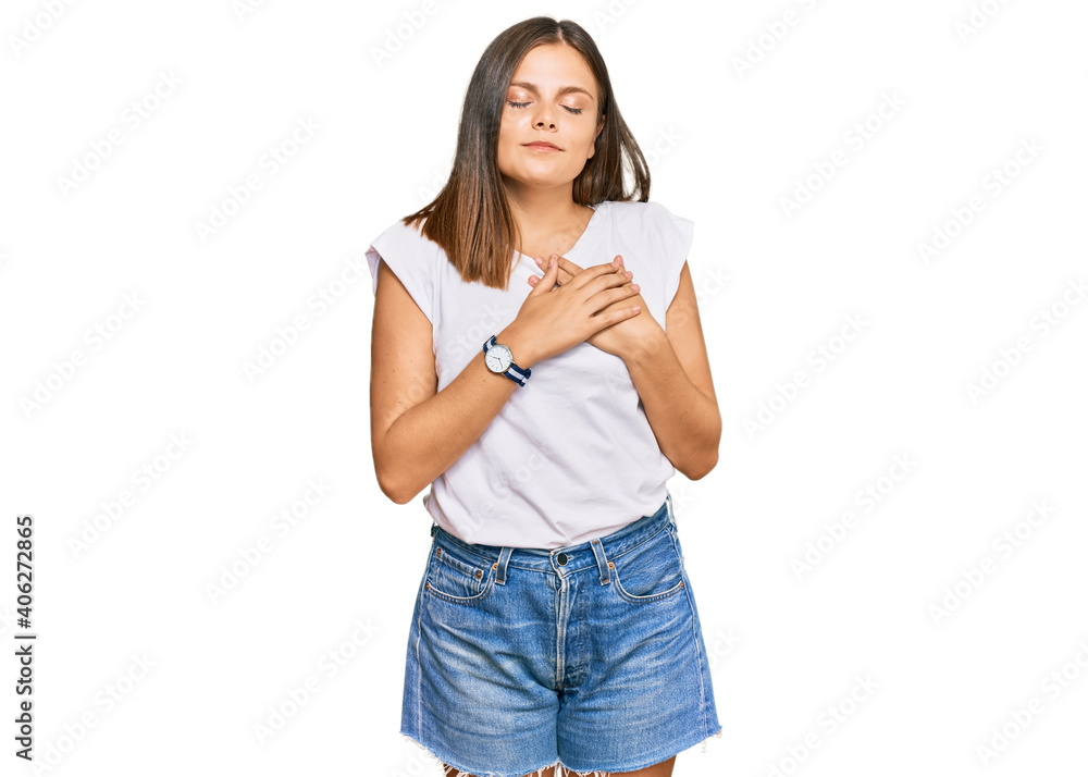 Young caucasian woman wearing casual white tshirt smiling with hands on chest with closed eyes and grateful gesture on face. health concept. Young caucasian woman wearing casual white tshirt smiling with hands on chest with closed eyes and grateful gesture on face. health concept.