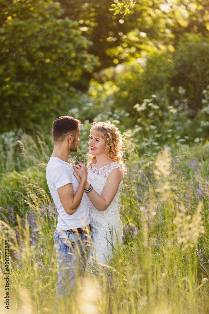 Young man and woman couple walk in the meadow. Tender holding each other. Spring lovestory. Blonde-haired girl with curled hairs and man weared in casual and denim. Young family Young man and woman couple walk in the meadow. Tender holding each other. Spring lovestory. Blonde-haired girl with curled hairs and man weared in casual and denim. Young family