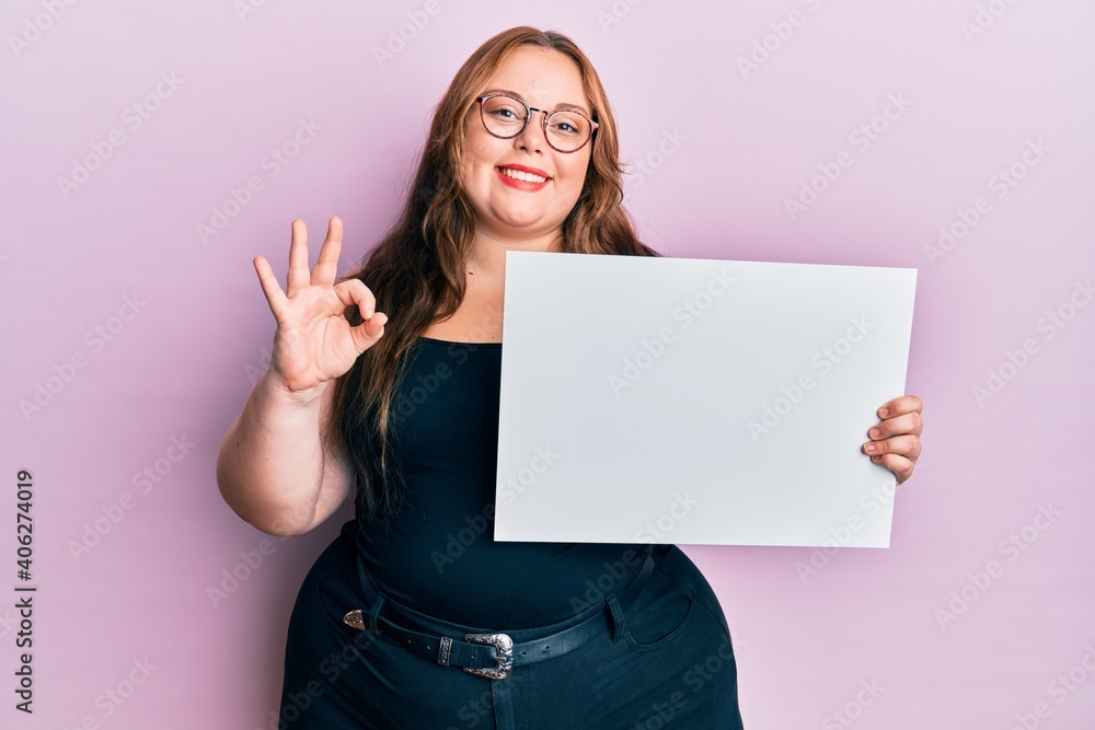 Naklejka premium Plus size caucasian young woman holding blank empty banner doing ok sign with fingers, smiling friendly gesturing excellent symbol
