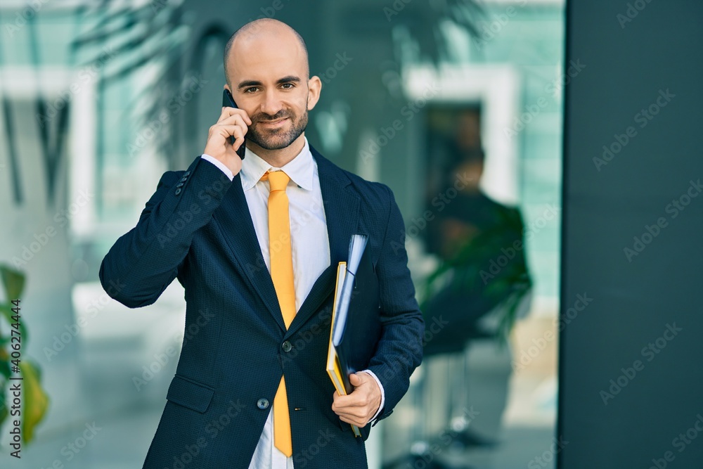 Young hispanic bald businessman smiling happy talking on the smartphone at the city. Young hispanic bald businessman smiling happy talking on the smartphone at the city.