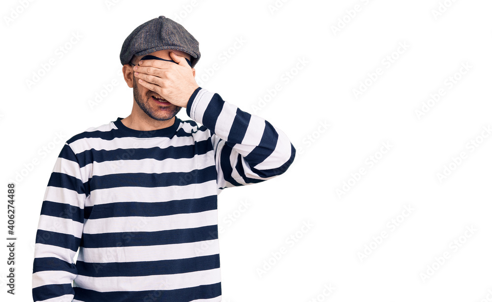 Young handsome man wearing burglar mask smiling and laughing with hand on face covering eyes for surprise. blind concept. Young handsome man wearing burglar mask smiling and laughing with hand on face covering eyes for surprise. blind concept.
