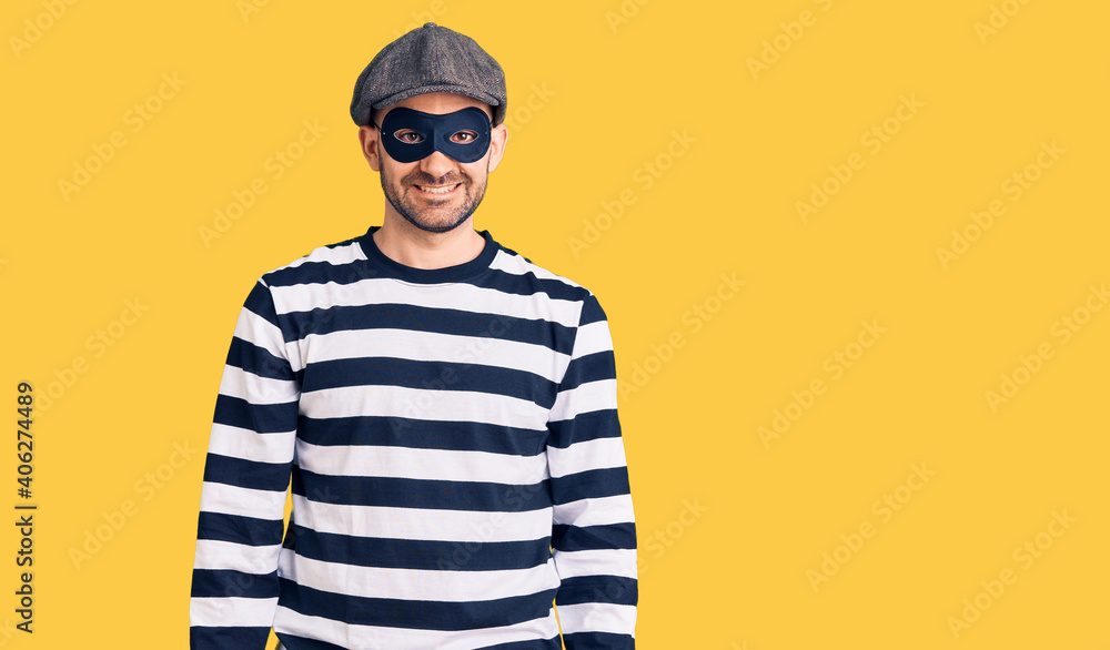 Fototapeta premium Young handsome man wearing burglar mask with a happy and cool smile on face. lucky person.