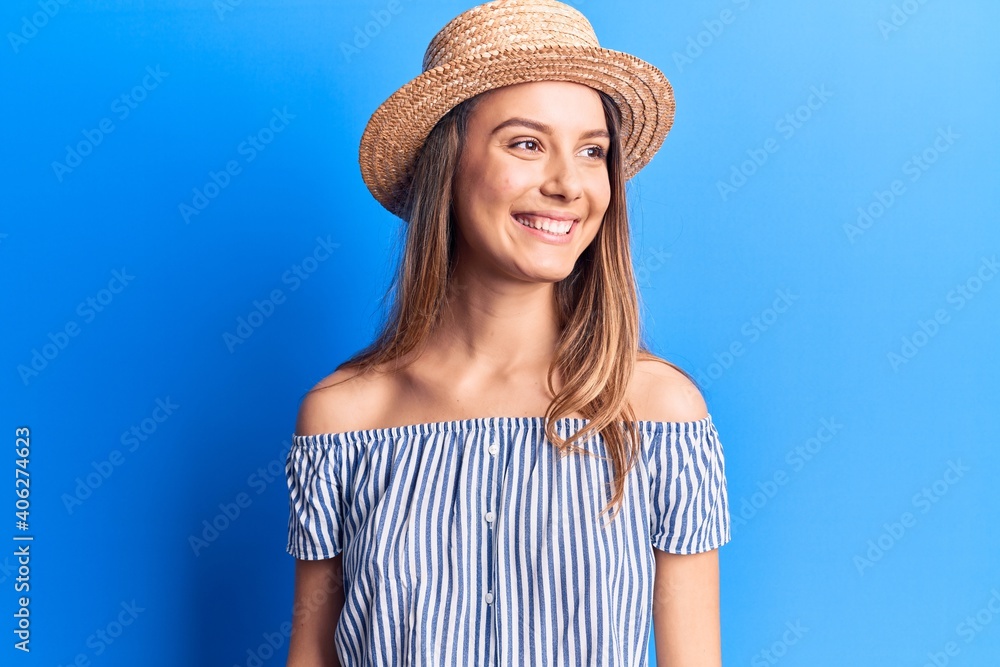 Young beautiful girl wearing summer hat and striped t-shirt looking to side, relax profile pose with natural face and confident smile.