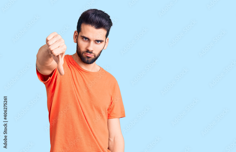 Young handsome man with beard wearing casual t-shirt looking unhappy and angry showing rejection and negative with thumbs down gesture. bad expression. Young handsome man with beard wearing casual t-shirt looking unhappy and angry showing rejection and negative with thumbs down gesture. bad expression.
