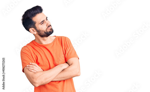 Young handsome man with beard wearing casual t-shirt looking to the side with arms crossed convinced and confident