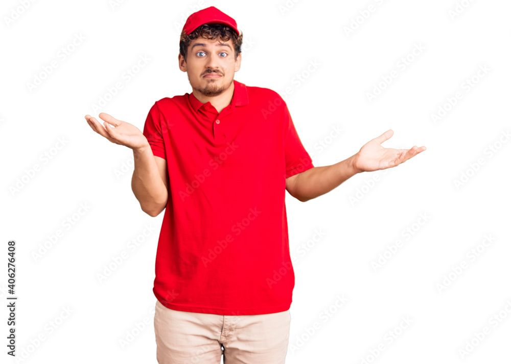 Young handsome man with curly hair wearing delivery uniform clueless and confused expression with arms and hands raised. doubt concept. Young handsome man with curly hair wearing delivery uniform clueless and confused expression with arms and hands raised. doubt concept.