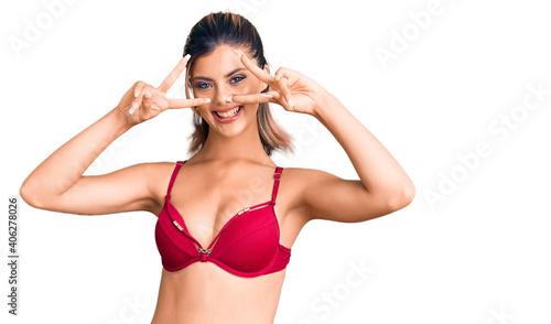 Young beautiful woman wearing bikini doing peace symbol with fingers over face, smiling cheerful showing victory