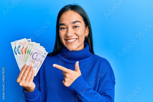 Photography Young asian woman holding singapore dollars banknotes smiling happy pointing wit