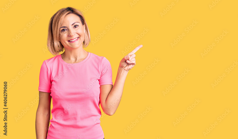 Young blonde woman wearing sportswear with a big smile on face, pointing with hand finger to the side looking at the camera. Young blonde woman wearing sportswear with a big smile on face, pointing with hand finger to the side looking at the camera.