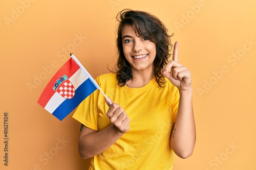 Young hispanic woman holding croatia flag smiling with an idea or question pointing finger with happy face  number one