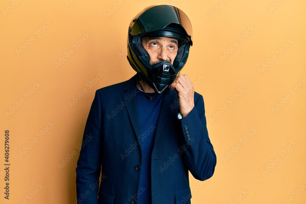 Middle age hispanic man wearing motorcycle helmet thinking concentrated about doubt with finger on chin and looking up wondering Middle age hispanic man wearing motorcycle helmet thinking concentrated about doubt with finger on chin and looking up wondering