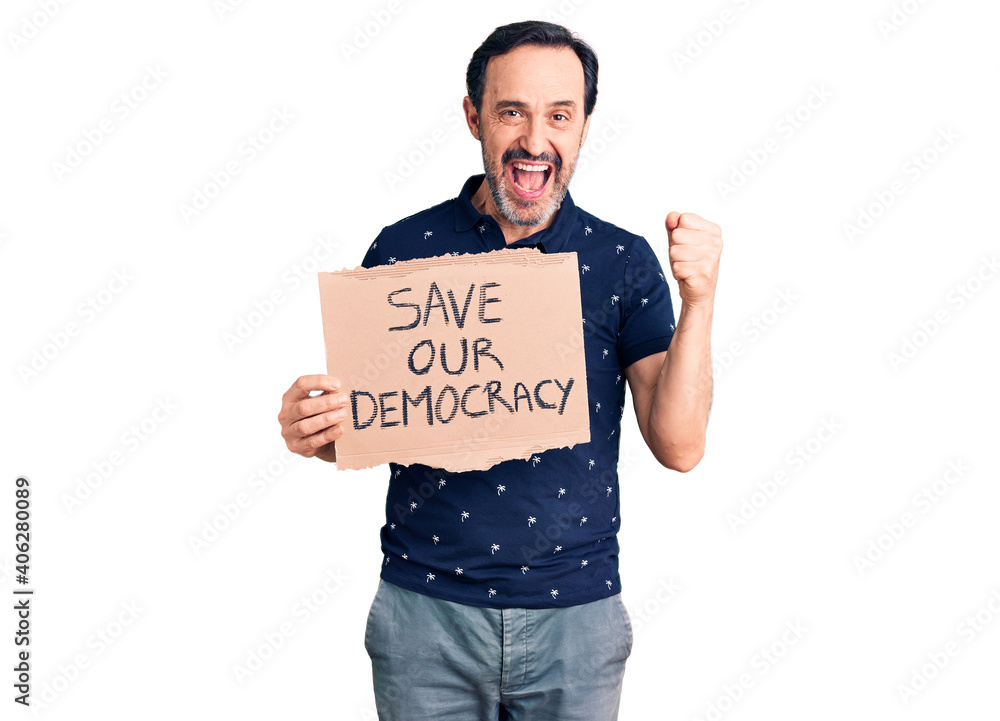 Middle age handsome man holding save our democracy cardboard banner screaming proud, celebrating victory and success very excited with raised arms Middle age handsome man holding save our democracy cardboard banner screaming proud, celebrating victory and success very excited with raised arms