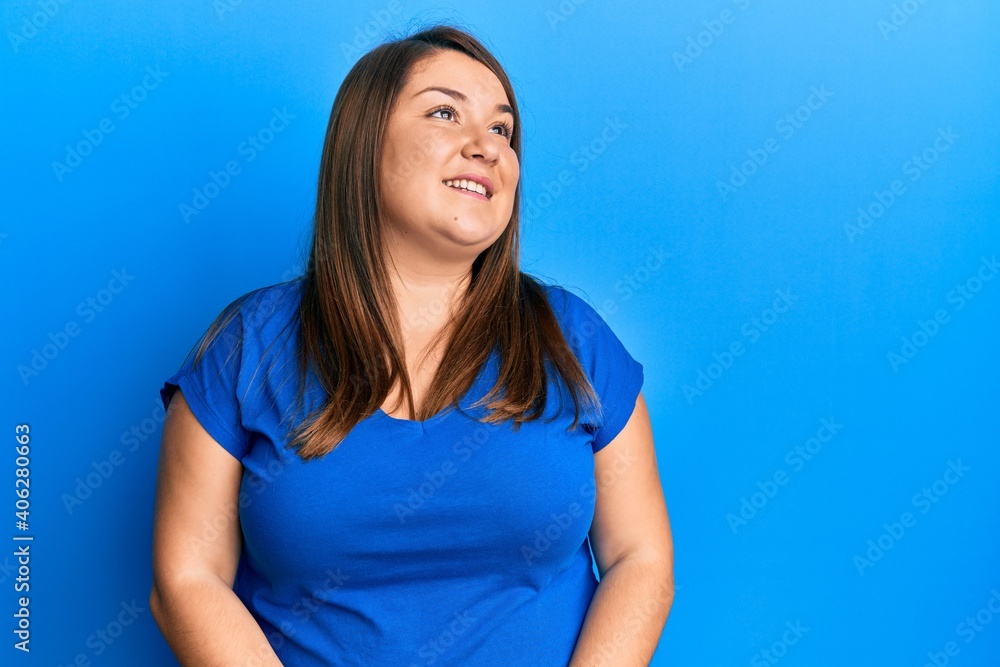 Beautiful brunette plus size woman wearing casual blue t shirt looking away to side with smile on face, natural expression. laughing confident. Beautiful brunette plus size woman wearing casual blue t shirt looking away to side with smile on face, natural expression. laughing confident.