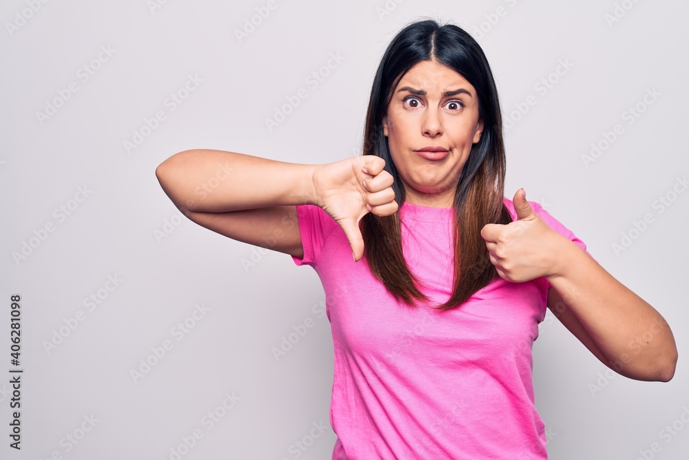 Young beautiful brunette woman wearing casual pink t-shirt standing over white background Doing thumbs up and down, disagreement and agreement expression. Crazy conflict Young beautiful brunette woman wearing casual pink t-shirt standing over white background Doing thumbs up and down, disagreement and agreement expression. Crazy conflict