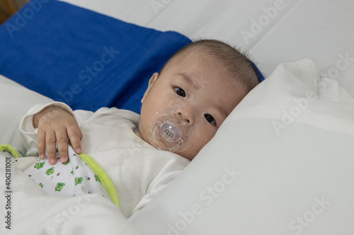 Illness asian baby boy lying down on sickbed and looking at camera, admitted in hospital and saline intravenous (IV) drip on hand. photo