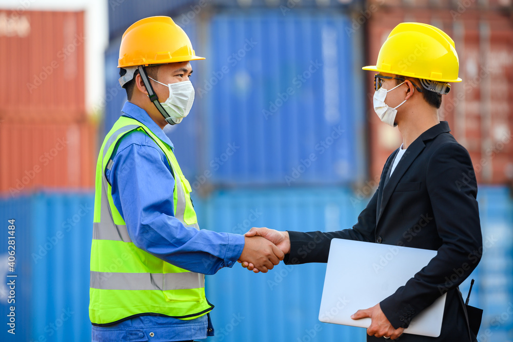 Businessmen and engineers wearing helmets and masks greet each other with a handshake and discuss unloading of container boxes from a cargo ship. Businessmen and engineers wearing helmets and masks greet each other with a handshake and discuss unloading of container boxes from a cargo ship.