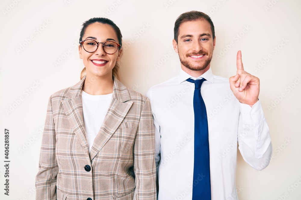 Beautiful couple wearing business clothes showing and pointing up with finger number one while smiling confident and happy. Beautiful couple wearing business clothes showing and pointing up with finger number one while smiling confident and happy.
