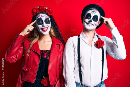 Couple wearing day of the dead costume over red smiling pointing to head with one finger  great idea or thought  good memory