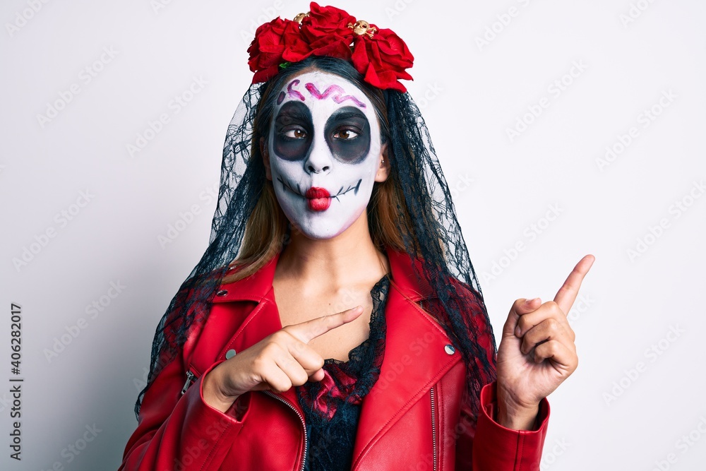 Woman wearing day of the dead costume pointing with fingers to the side making fish face with mouth and squinting eyes, crazy and comical. Woman wearing day of the dead costume pointing with fingers to the side making fish face with mouth and squinting eyes, crazy and comical.