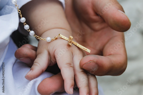 Man's hand holding the hand of a baby, on the day of his christening and with a medal of the cross.