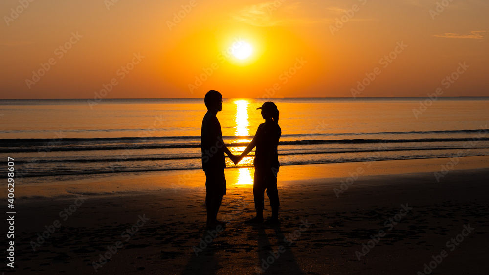 Romantic couple on the beach at colorful sunset on background.