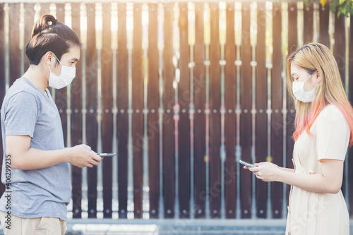 Young asia couple using smart mobile phote outdoor wearing face mask during coronavirus outbreak - Millennial couple watching videos on smartphone - Social distance and technology concept photo