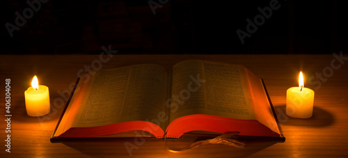 Bible and lit candles on a table.  Holy bible  and candles lit  in dark photo