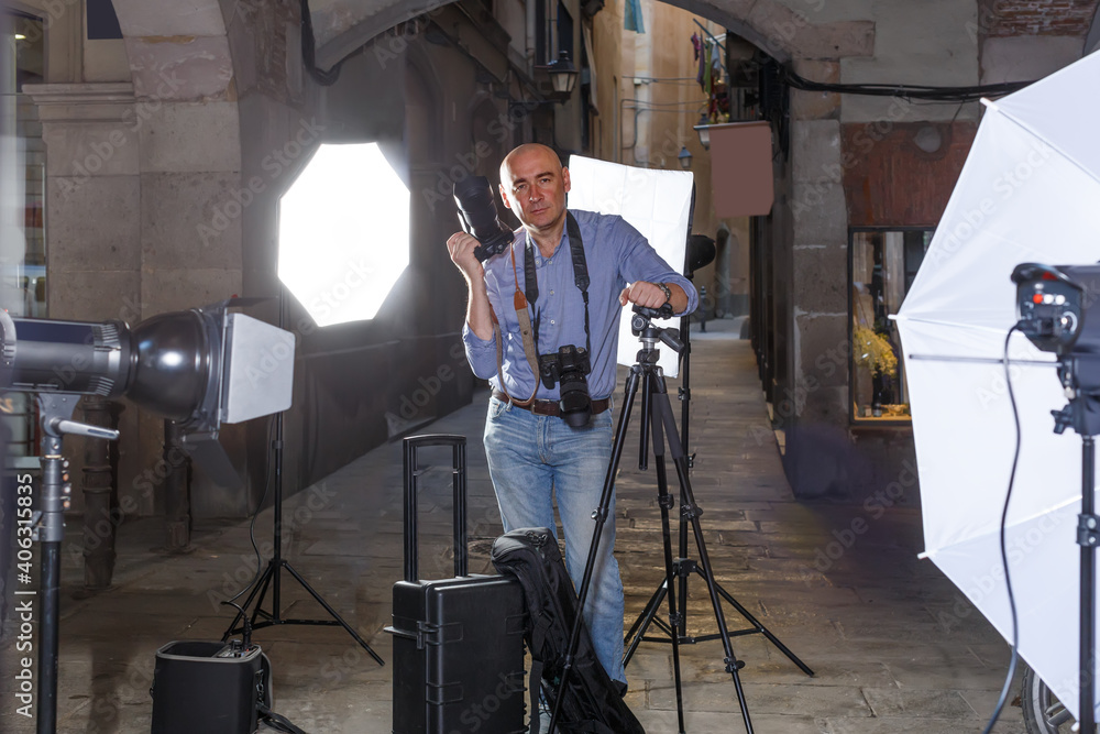 Portrait of positive photographer with his camera during professional photo shooting on town street