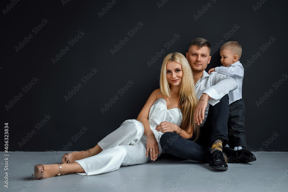 Photo of a beautiful European married couple, a young girl and a guy with a little son, posing together in front of the camera. Black background, concept of modern family, family relationships.