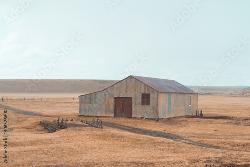 Gold Wheat flied panorama with house and agricultural tools. rural countryside. Empty Countryside scene featuring old farms barn on grassy hill with a summer sky on background and yellow grass around