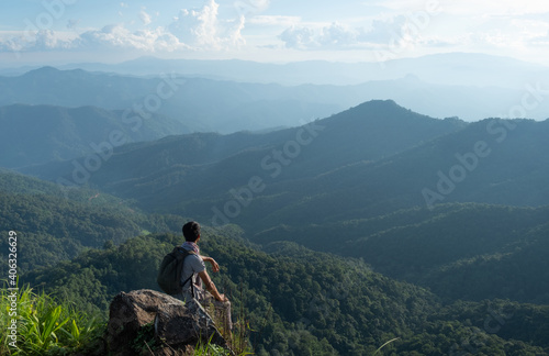 young man sit on the rock, looking at the top of the mountain.