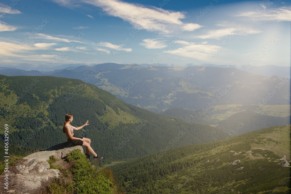 A girl sits on the edge of the cliff and looking at the sun valley and mountains