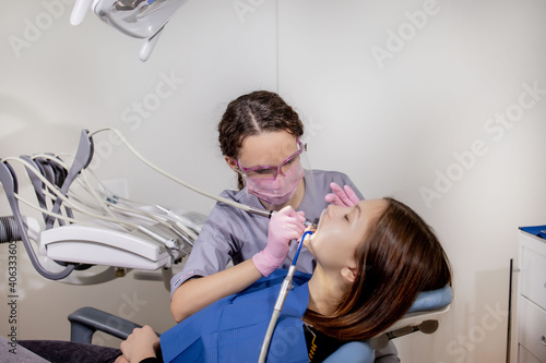 Adult woman visiting a dental office. Dentist hands in rubber protective gloves using white polishing stone for patient