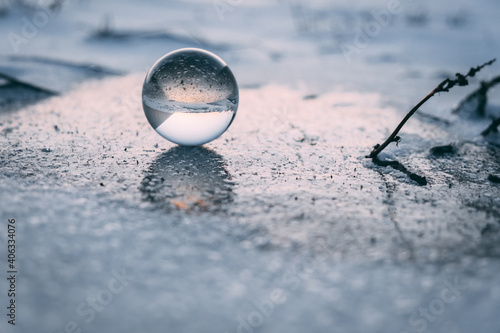 glass transparent ball on an ice crust in winter, reflected on ice. dawn
