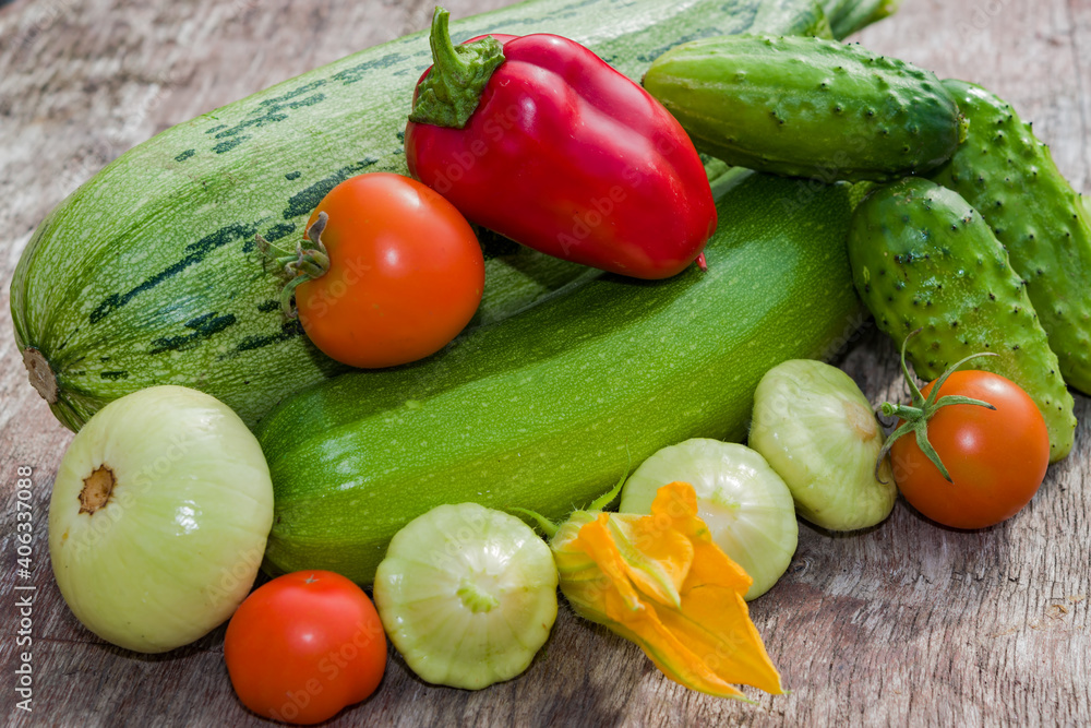 A pile of fresh vegetables on a wooden table. Harvest green zucchini, cucumbers, squash, red tomatoes, sweet peppers, illuminated by the sun. A pile of fresh vegetables on a wooden table. Harvest green zucchini, cucumbers, squash, red tomatoes, sweet peppers, illuminated by the sun.