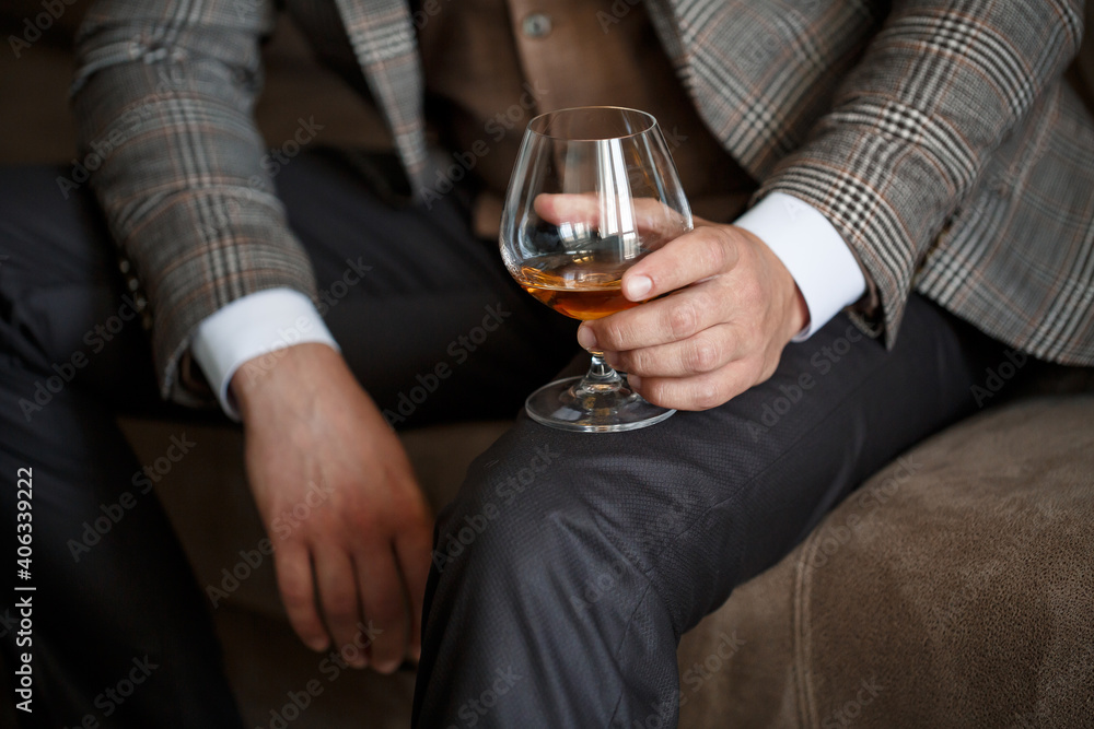 A man businessman holds a glass with alcohol in his hand. Dressed in a jacket and shirt. Rest after a working day