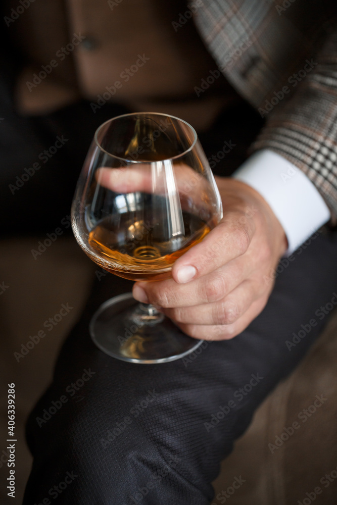 A man businessman holds a glass with alcohol in his hand. Dressed in a jacket and shirt. Rest after a working day A man businessman holds a glass with alcohol in his hand. Dressed in a jacket and shirt. Rest after a working day