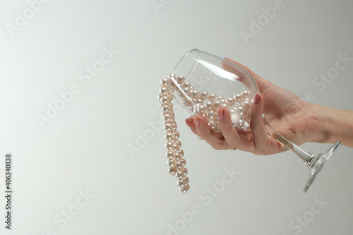 Creative photo beautiful female hand holds an empty glass with pearl beads inside on a gray background. High quality photo