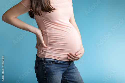 a young pregnant woman holds her lower back and her stomach with her hands