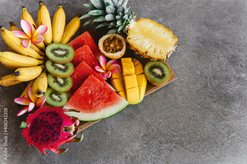 Tropical fruits assortment on a wooden plate. Stone background. Top view. Copy space.