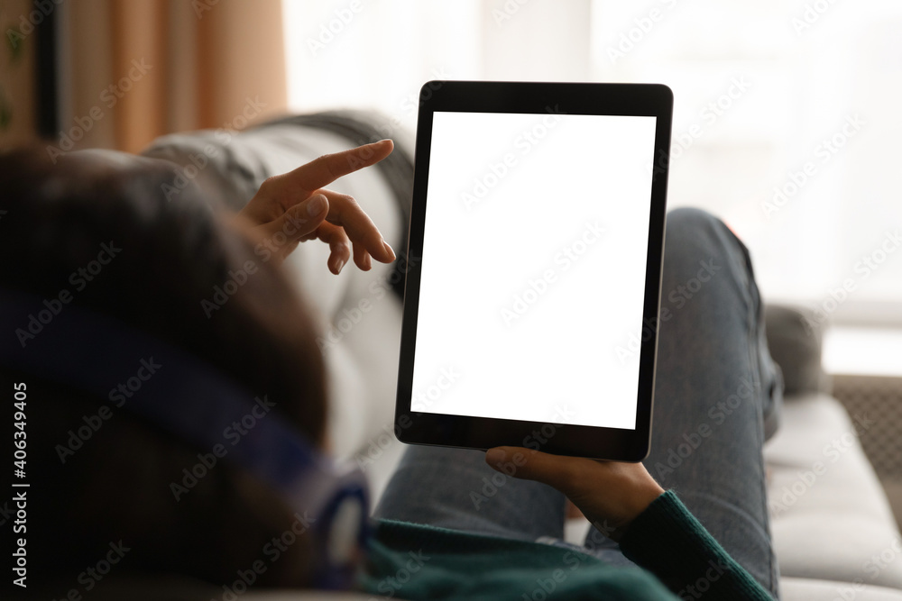 Close up back view of woman lying relaxing on sofa at home use modern tablet gadget. Female rest on couch look at white empty mockup screen on pad device. Technology, communication concept.